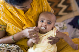 Getting her first spoon-ful of Rice. This is very soft boiled rice, some sugar and ghee. Notice the custom made silver spoon - spiffy eh!